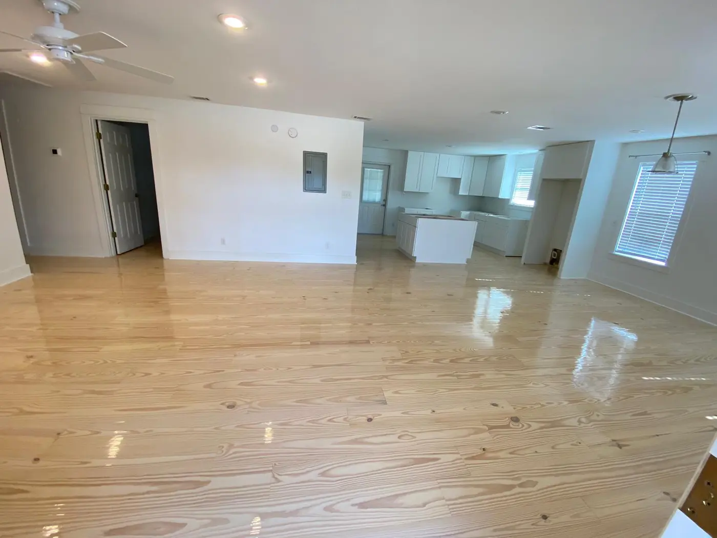 Open-plan living area with a high-gloss wood floor and a new white kitchen